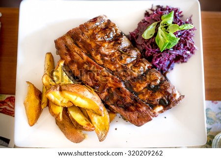 Barbecue pork ribs as main dish at restaurant. Pork delicacy with delicious barbecue sauce, parsley, cabbage and potatoes