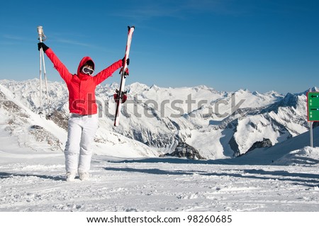 excited girl standing on top of the mountain with skis and sticks in her hands on a sunny winter day