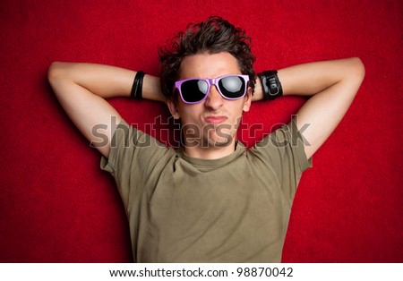 male model making strange faces on red background, wearing purple sunglasses. isolated