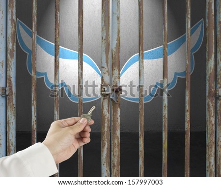 Hand hold key unlocking locked door with blue and white wings in gray concrete background