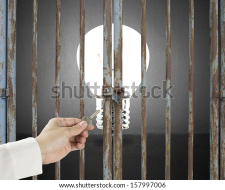 Hand hold key opening locked door with lighting bulb in gray concrete wall background