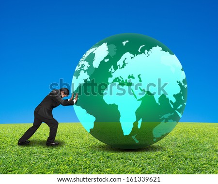 businessman rolling large green ball with global map on it with green meadow and clear blue sky background