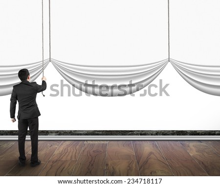 businessman pulling open blank curtain with empty white background behind on wooden floor