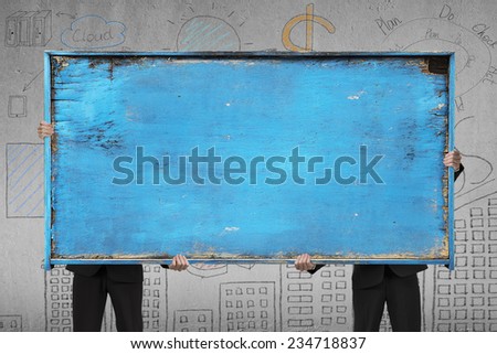 two businessman holding old blue blank wooden noticeboard on doodles wall background