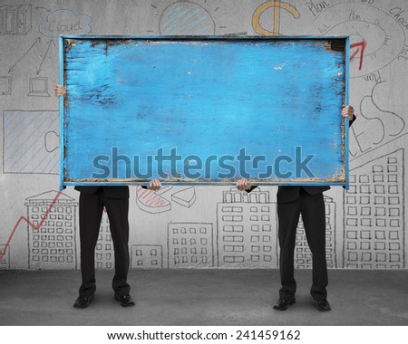 two businessman hold old blue blank wooden billboard stand on concrete floor with doodles wall background