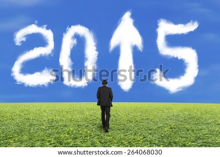 Businessman walking for white 2015 year shape cloud with arrow up sign and blue sky grass background