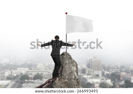 Businessman walking and balancing on old iron chain toward white flag of mountain peak with cityscape background