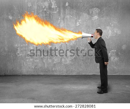 Angry businessman screaming into megaphone spitting fire flame with concrete indoor background