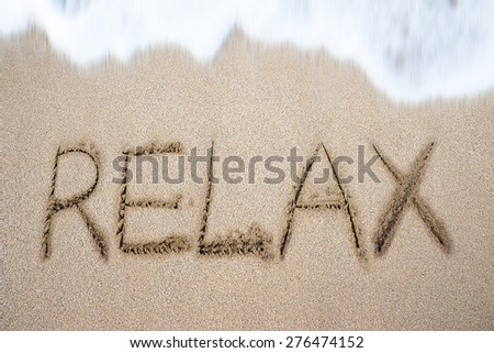 Relax word handwritten in sand on beach with white wave foam