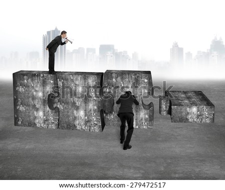 Boss using speaker yelling at employee pushing big jigsaw puzzle concrete blocks, on concrete floor with cityscape skyline background