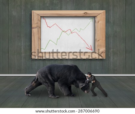 Businessman fighting against black bear with two trend lines of whiteboard, on wooden indoors background.