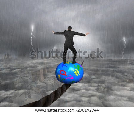 Businessman standing on top of colorful symbols ball, balancing on a wire, with heavy rain lightning overcast cityscape background.