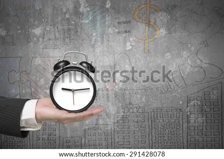 Hand holding alarm clock with business concepts doodles concrete wall background