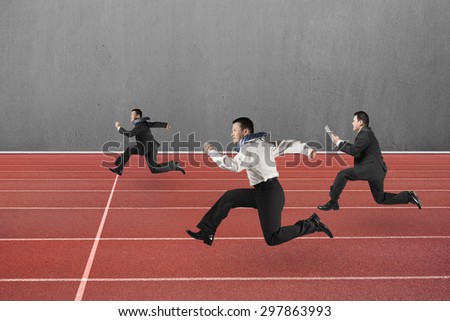 Three businessmen running on red track, with gray concrete wall background.