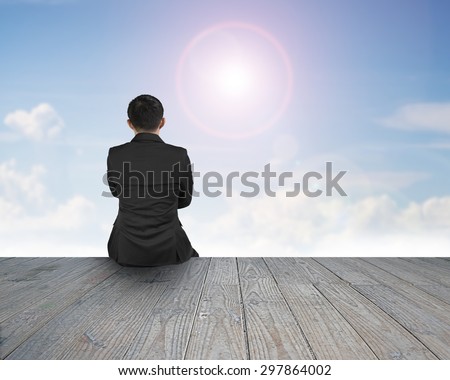 Rear view of black suit man sitting on wooden floor with natural sky sunlight cloudscape background.