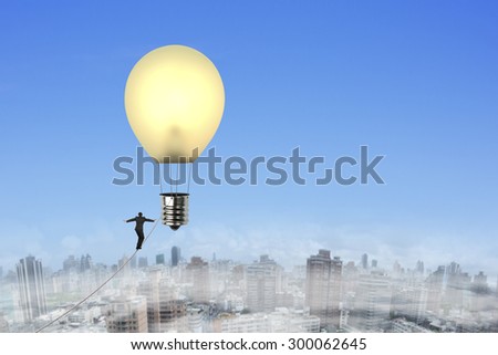 Businessman walking tightrope toward yellow lightbulb shape hot air balloon, with natural sky urban scene background.