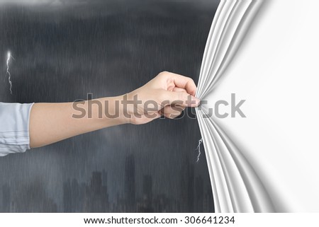 Female hand pulling open blank white curtain covering stormy city.