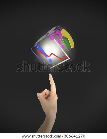 Human index finger pointing at illuminated transparent box of business graphs, on black background.