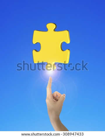 Human index finger pointing at gold jigsaw puzzle piece, on blue background.