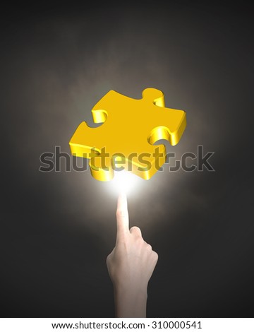 Human index finger pointing at gold jigsaw puzzle piece with bright light, on black background.