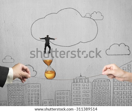 Two hands pulling rope with businessman balancing on hourglass, on hand-drawn doodles concrete wall background.