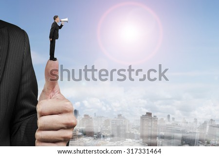 Businessman using speaker shouting on another man big hand thumb, with sun sky clouds cityscape background.