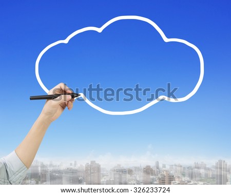 Female hand holding pen drawing white cloud in sky, side view, with city buildings background.