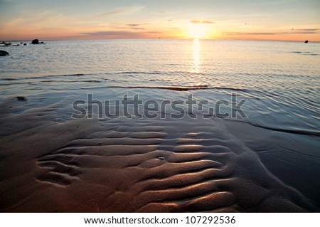Golden sunset on the sea. Coastal landscape with setting Sun reflections on the water and sand