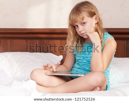 Little blond girl seat in the bed with tablet computer