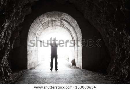 Man stands in dark tunnel with glowing end
