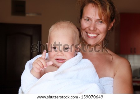 Young Caucasian mother holds with smile her baby in white cotton towel after the bath