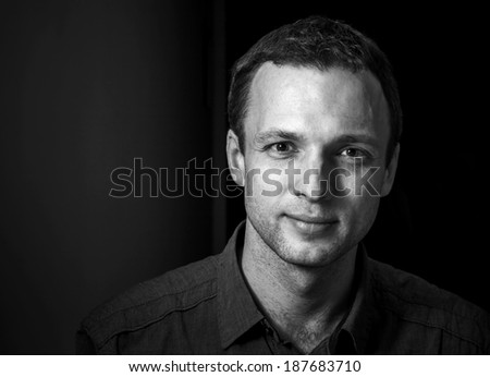 Monochrome portrait of young smiling Caucasian man on black background