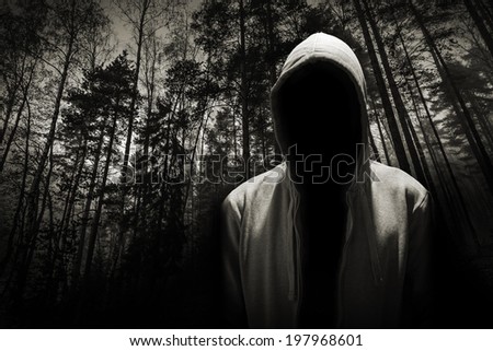 Portrait of dangerous man hiding under the hood in the forest