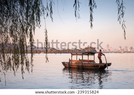 Hangzhou, China - December 5, 2014: Traditional Chinese wooden recreation boat with boatman floats on the West Lake. Famous park in Hangzhou city center, China