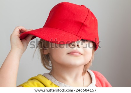 Studio portrait of funny baby girl in red baseball cap over gray wall background