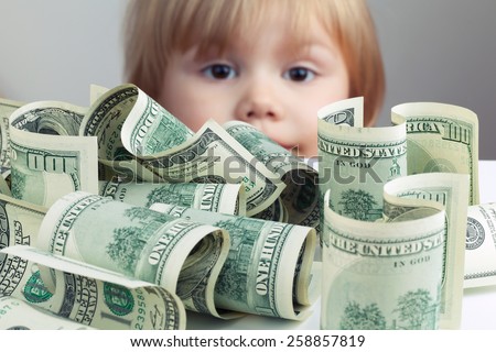 Pile of United States dollar hundred USD banknotes on white table and blurred baby looking on it on a background. Retro tonal correction photo filter effect, selective focus on money