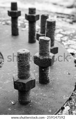 Big black steel bolts and nuts in a circle on rusted industrial cover. Selective focus