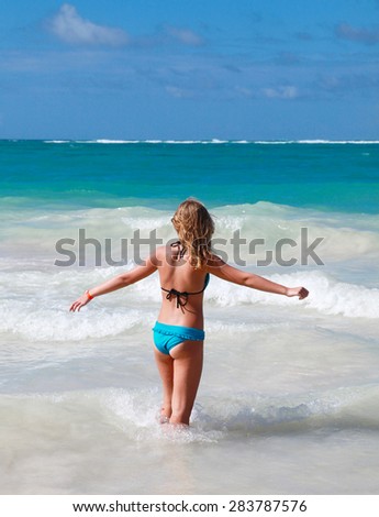 Happy teenage girl goes in the ocean water under deep blue sky, back view