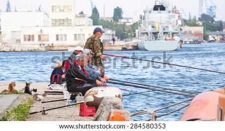 Varna, Bulgaria - July 20, 2014: Senior fishermen catch fish from the shore, group of cats waiting for haul