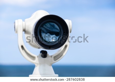 White paid telescope stands on sea coast over blue sky background