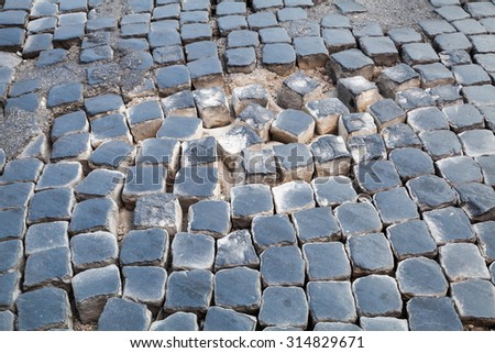 Damaged cobblestone road pavement with sand backdrop