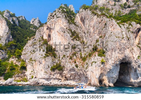 Coastal rocks of Capri island, small pleasure motorboat with tourists go near the coast