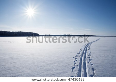 Sun, snow and Ski track crossing a frozen lake. Winter sport - cross-country skiing.