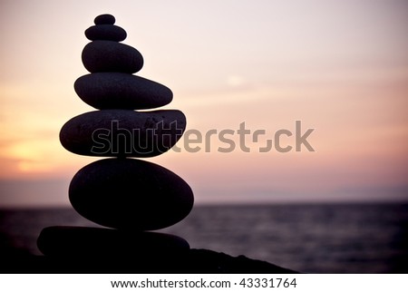 A stack of rocks balance on a log with the sunset in the distance.
