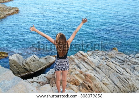 Young woman stands on rocks and looking at sea with her hands up. The concept of freedom and dreams. Costa Brava, Spain.