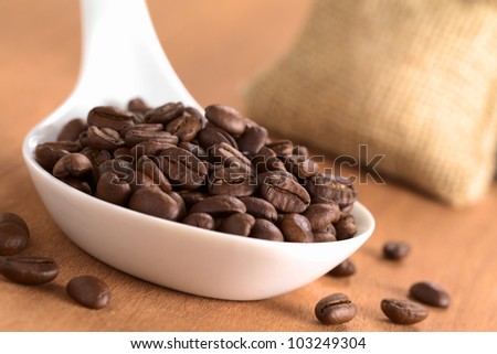 Roasted Peruvian coffee beans on ceramic spoon with jute sack in the back (Selective Focus, Focus on the coffee beans one third into the spoon)