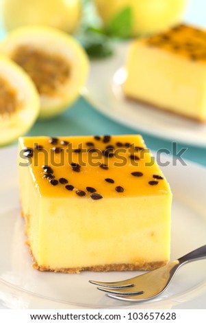 Fresh passion fruit cheesecake dessert on plate with pastry fork with another cake and yellow passion fruits in the back (Selective Focus, Focus on the left upper front edge of the cake)