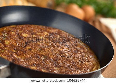 Preparing Spanish tortilla (omelette with potatoes) in frying pan with eggs and bread slices in the back (Selective Focus, Focus one third into the pan)