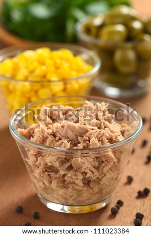 Canned tuna in glass bowl with fresh salad ingredients (sweet corn, green olives and watercress) in the back (Selective Focus, Focus one third into the tuna)