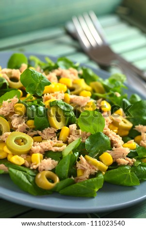 Fresh tuna, sweetcorn, green olive and watercress salad with fork and knife in the back (Selective Focus, Focus in the middle of the salad)
